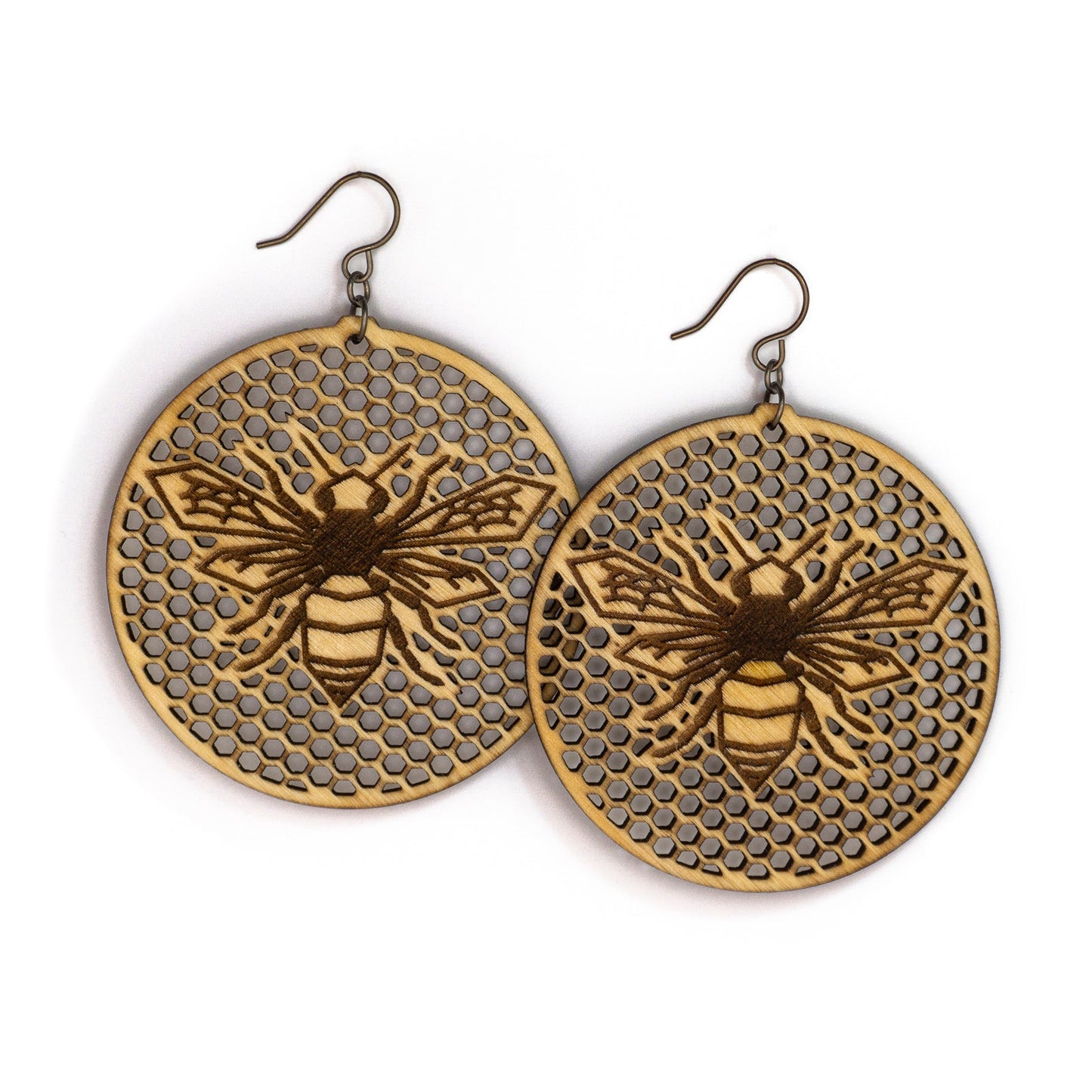 Two large round birch wood earrings, each depicting a laser etched honey bee on a background of many tiny hexagon holes. The bee is in flight as though viewing from above, it's wings spanning left to right and body positioned vertically up the center of the round discs.