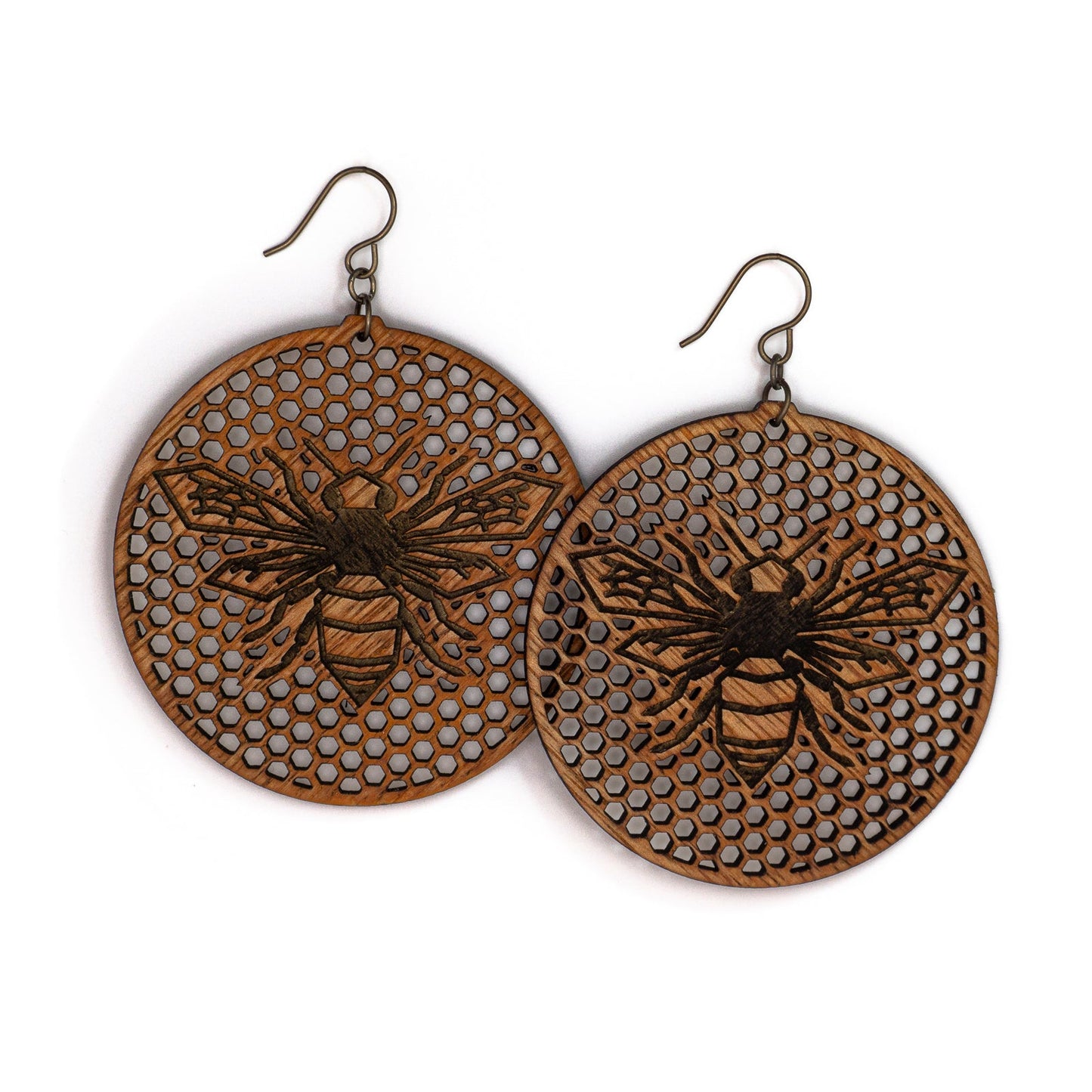 Two large round mahogany wood earrings, each depicting a laser etched honey bee on a background of many tiny hexagon holes. The bee is in flight as though viewing from above, it's wings spanning left to right and body positioned vertically up the center of the round discs.