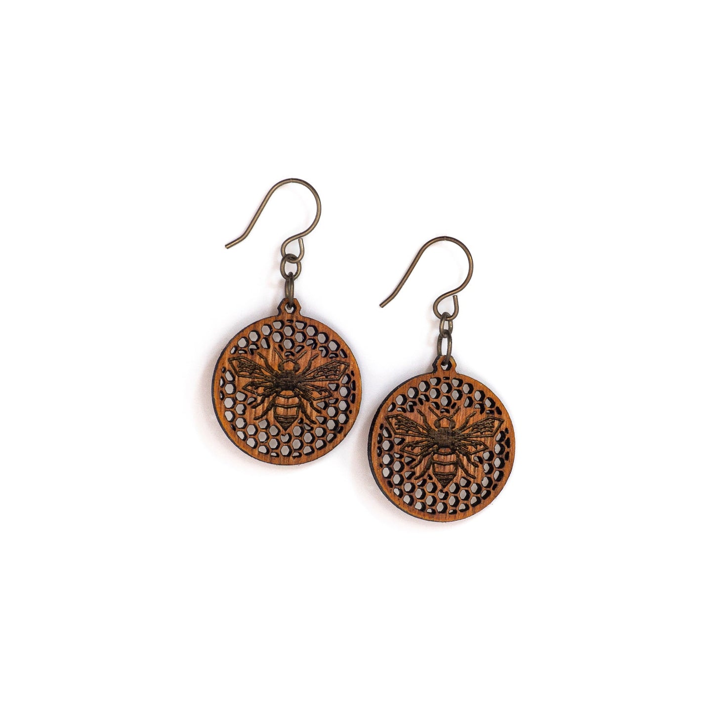 Two small round mahogany wood earrings, each depicting a laser etched honey bee on a background of many tiny hexagon holes. The bee is in flight as though viewing from above, it's wings spanning left to right and body positioned vertically up the center of the round discs.