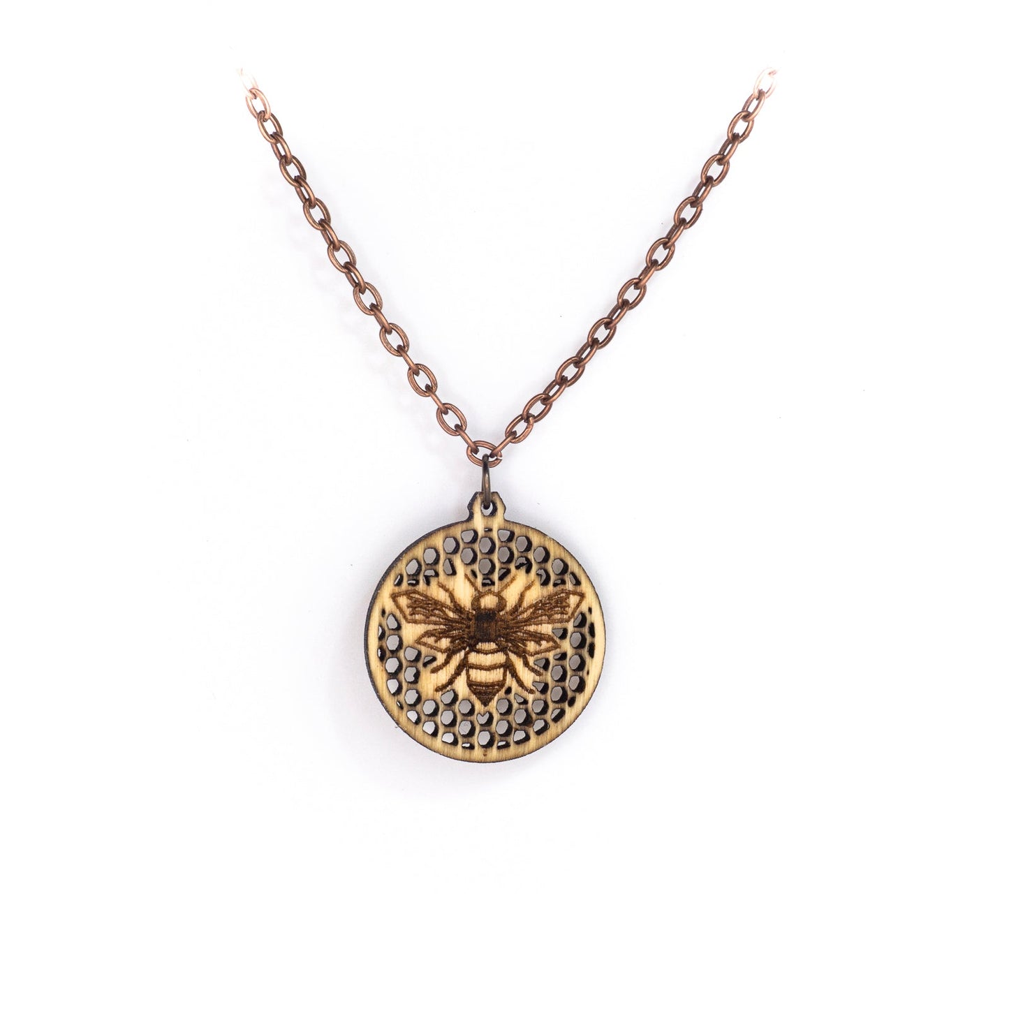 A delicate copper chain hangs in a 'V' shape. At its apex hangs a small round birch wood pendant, upon its face a laser etched honey bee on a background of many tiny hexagon holes. The bee is in flight as though viewing from above, it's wings spanning left to right and body positioned vertically up the center of the pendant.