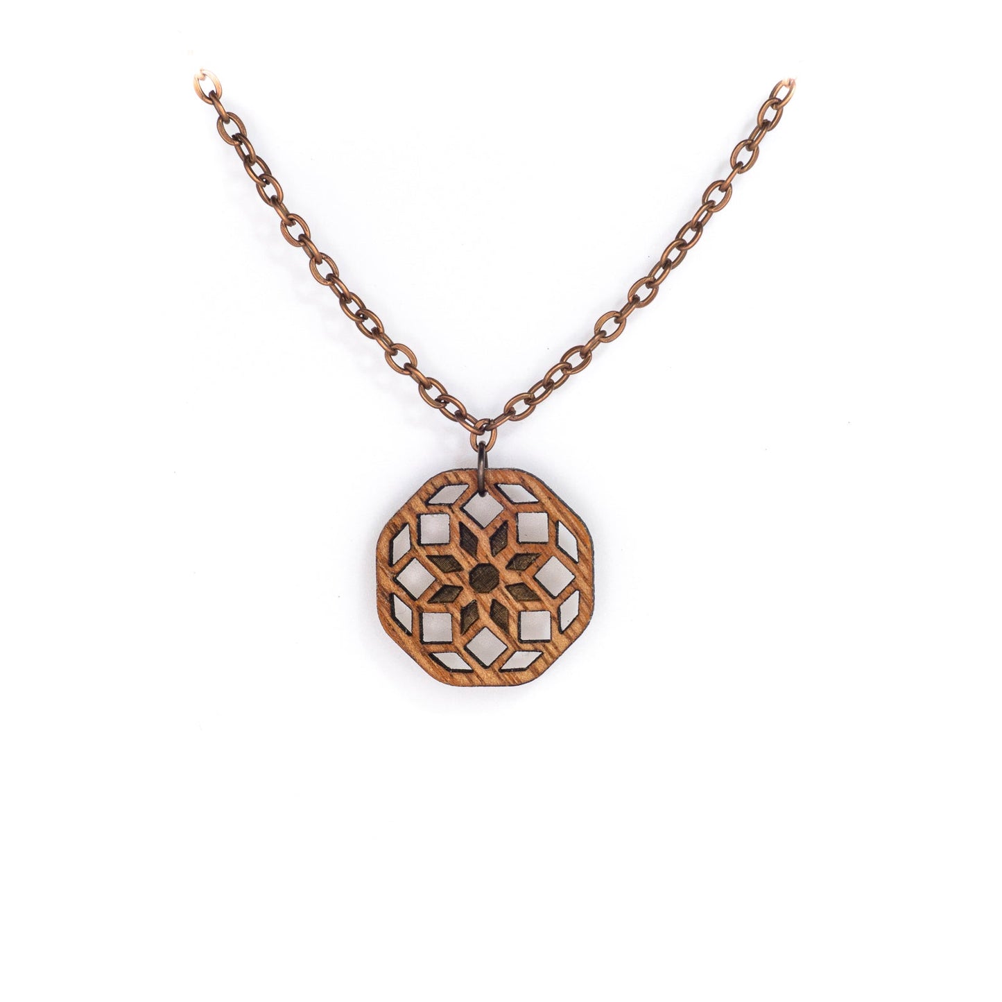 A delicate copper chain hangs in a 'V', at its apex is a small hexagonal mahogany wood pendant with a laser cut design. The design is illustrative of sacred geometry the cross-sectional lines forming an eight pointed flower at the center with two rows of diamonds emanating from it.